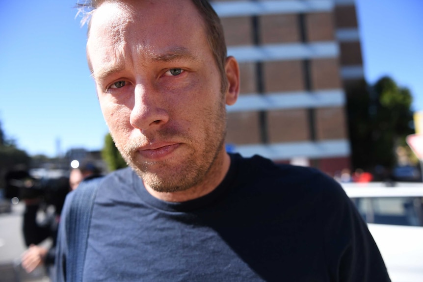 A close of a man in his late thirties in a navy t-shirt looking tired.
