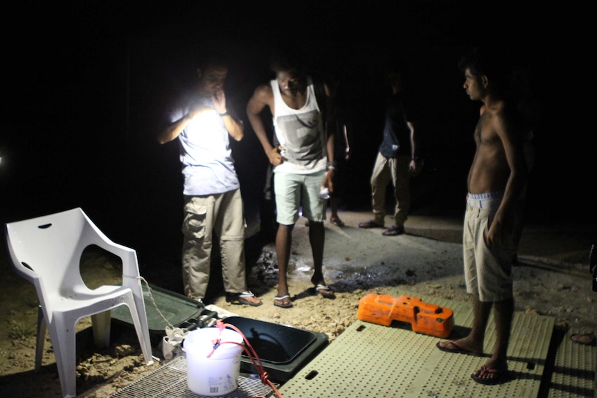 One man shines a torch as others peer into a well at night.