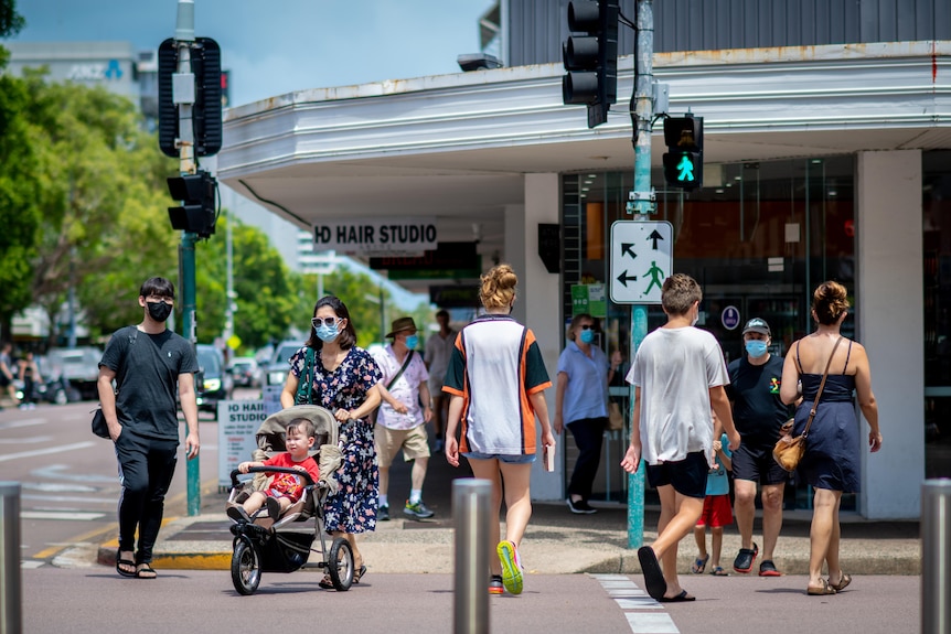 People cross a busy street in Darwin's CBD, everyone is wearing a mask.