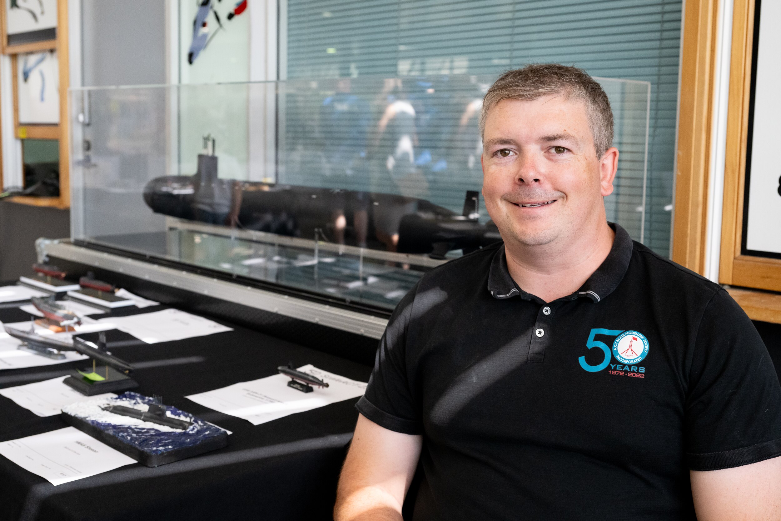 Man wearing a black shirt sitting beside a large submarine model.