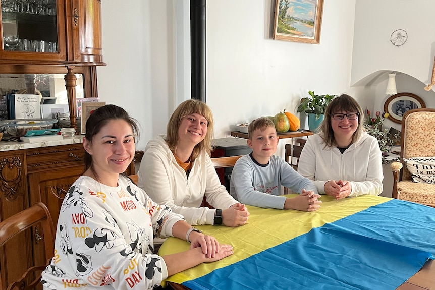 Oksana, her son and two friends sit around the dinner table. The flag of Ukraine is spread across the table. 