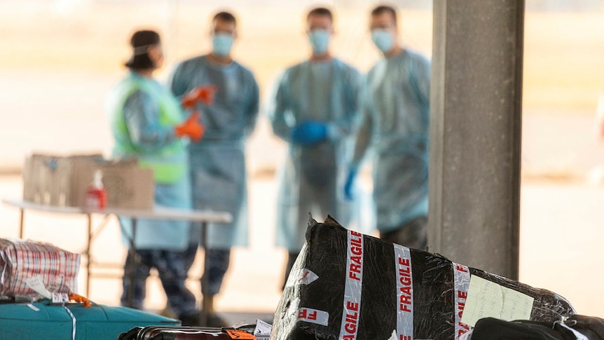 Workers in PPE stand by luggage from a repatriation flight. 