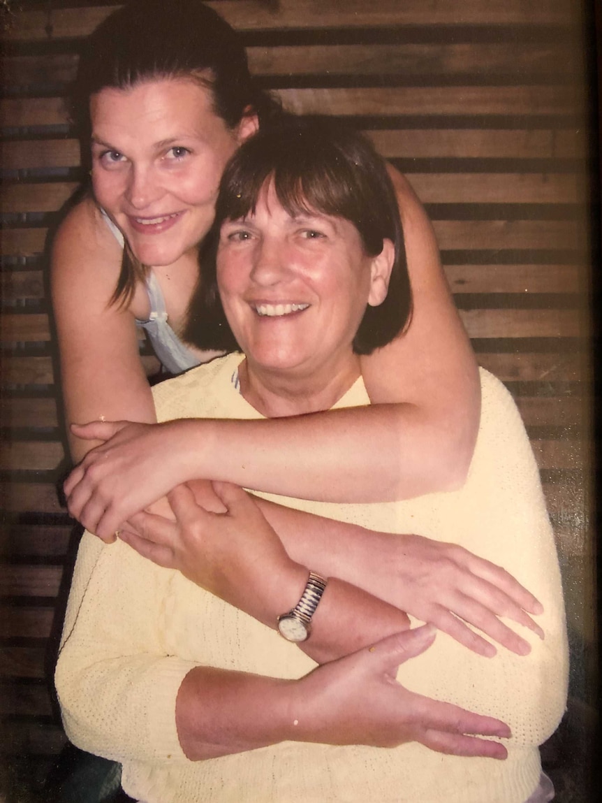 A young woman hugging an older woman from behind, both are smiling