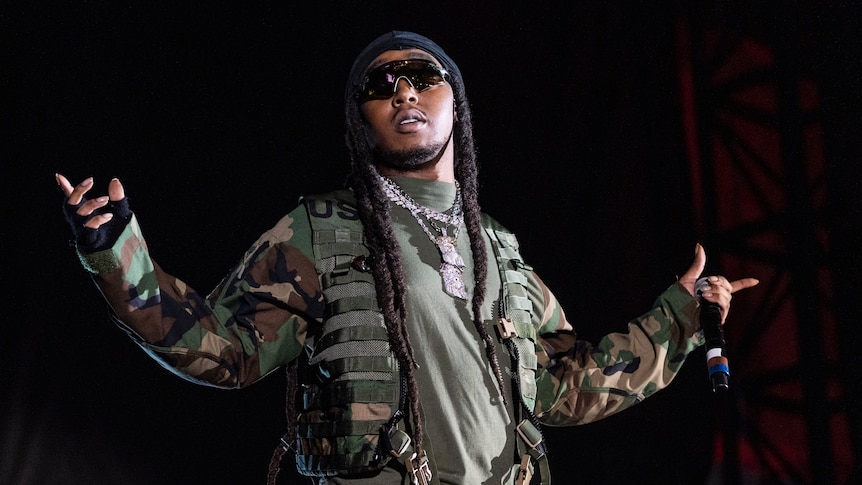 Takeoff of Migos performing live dresed in an army jacket with his arms oustretched