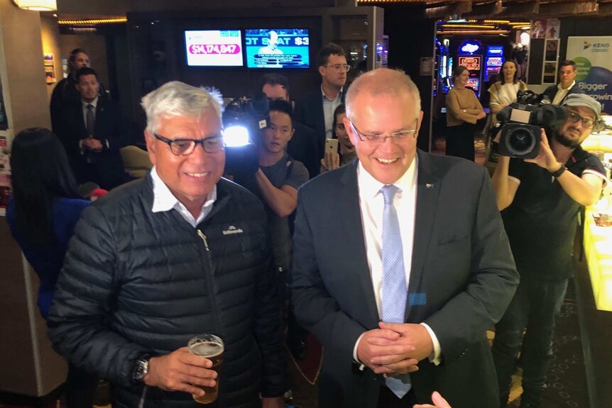 Liberal candidate for Gilmore Warren Mundine holds a beer in a pub while standing next to Prime Minister Scott Morrison.