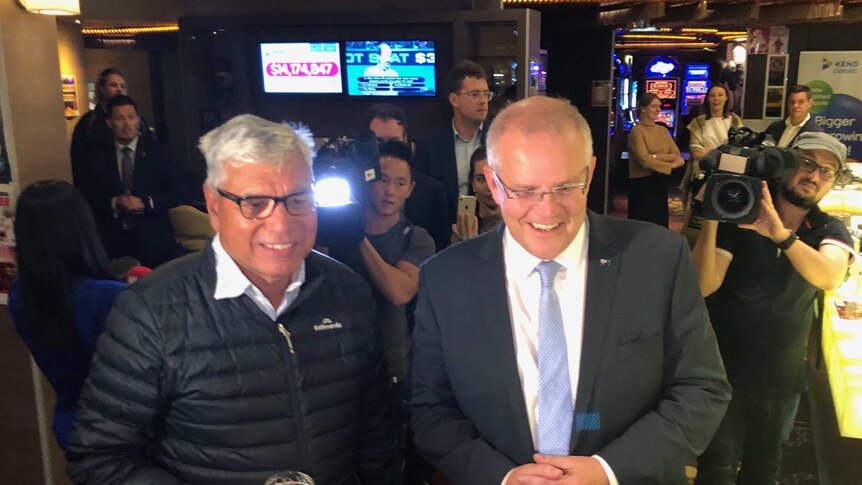 Liberal candidate for Gilmore Warren Mundine holds a beer in a pub while standing next to Prime Minister Scott Morrison.