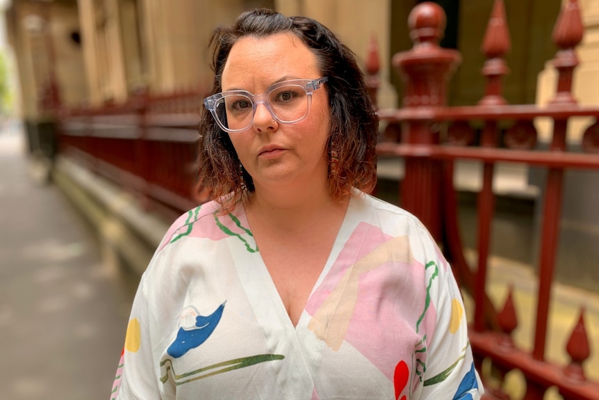 A woman with shoulder-length hair and classes standing in front of a courthouse.