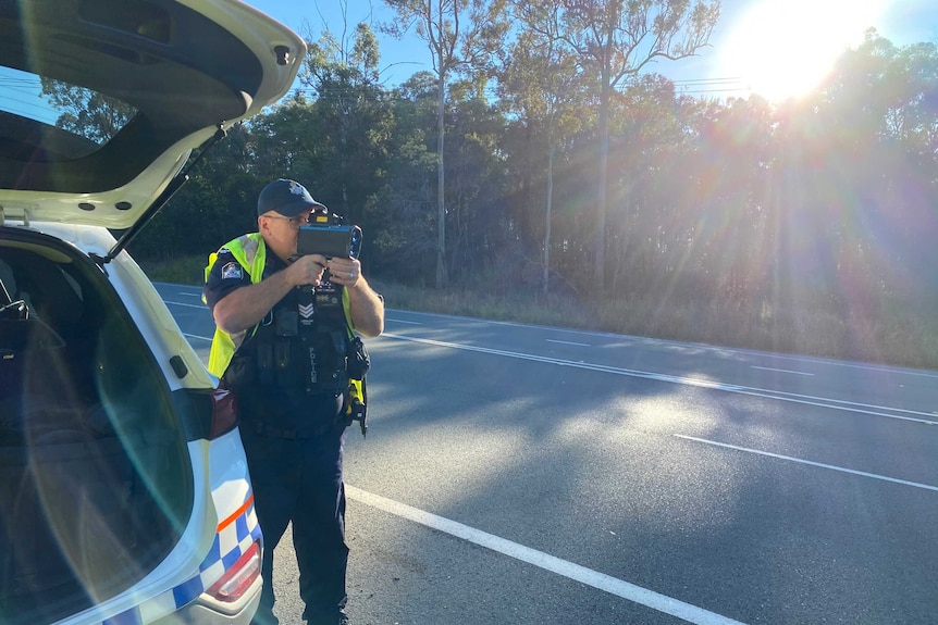 A police officer looks through a speedometer on a road.