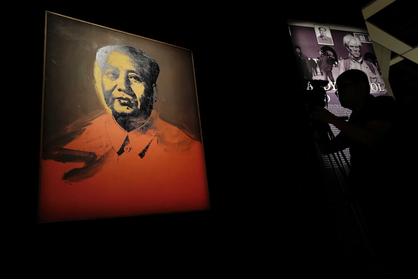 A cameraman stands in front of a painting Mao by US pop artist Andy Warhol.