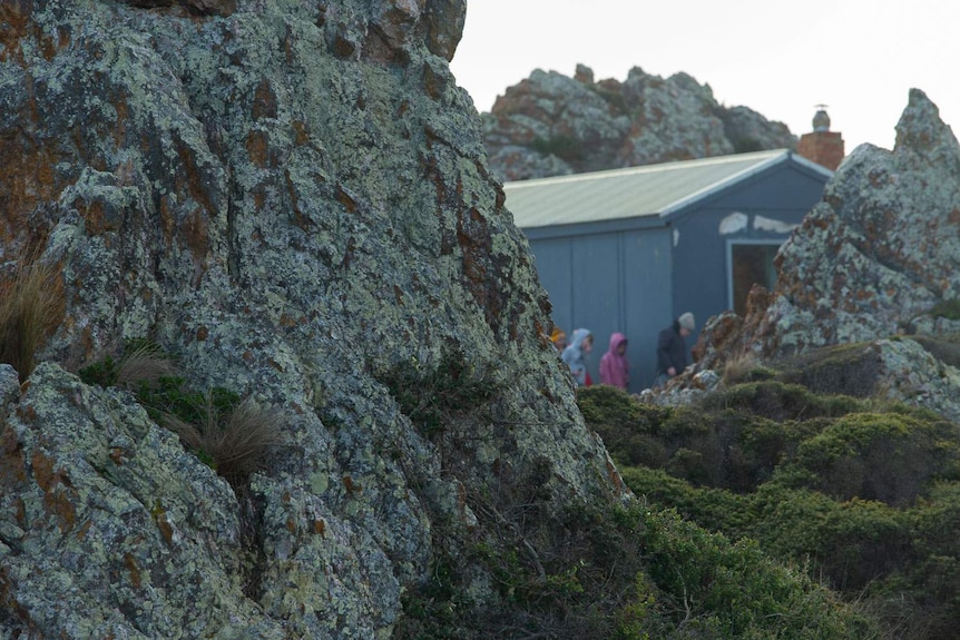 The visiting kids walk around a hut, tucked between large coastal rocks
