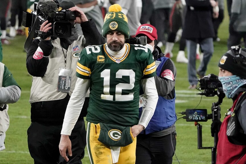 A dejected NFL quarterback is followed by TV cameras as he trudges off the field after a loss.