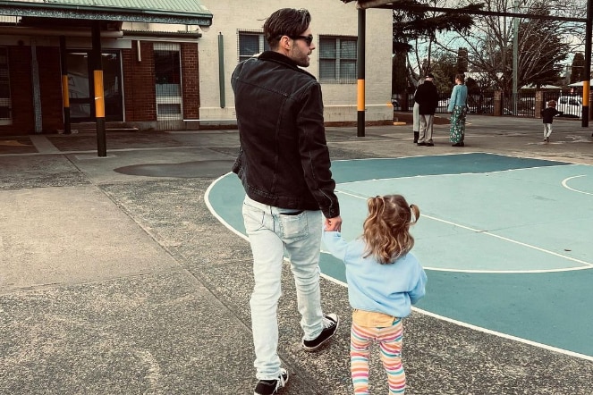 Benjamin Hampton facing away from the camera with his young daughter to his right in a playground