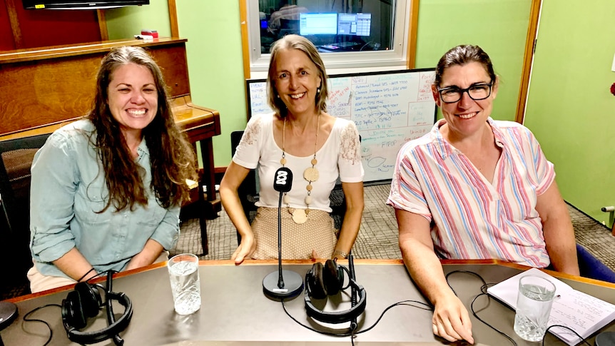 Three women behind microphones in a radio studio. 