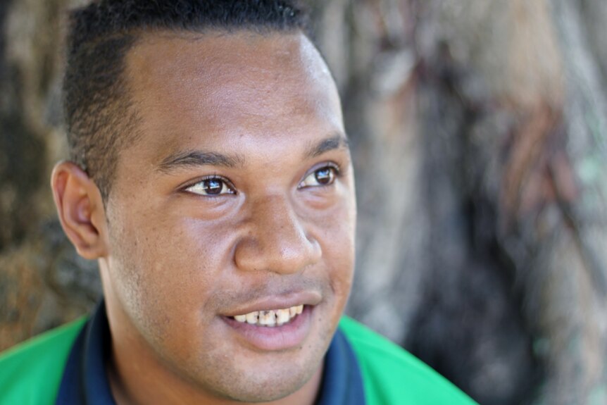 A young PNG man in a green shirt gazes into the distance.