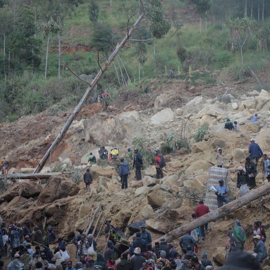 Dozens of people clamber of large boulders and soil searching for people trapped under rubble