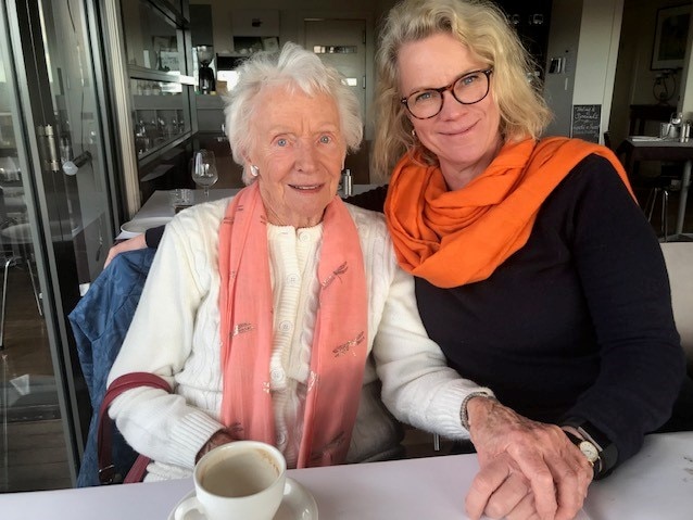 Two women sit at a table and smile as they pose for a photograph.