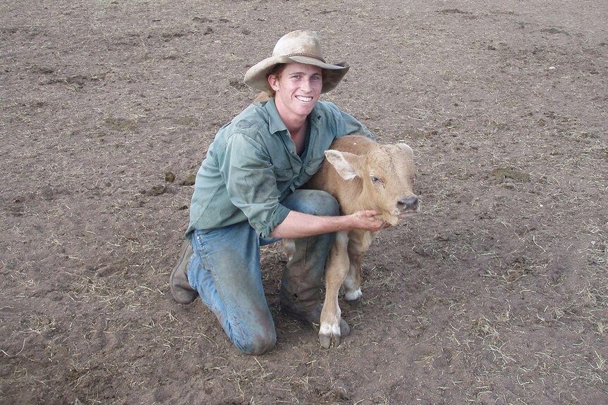 A young man crouches down to cuddle a calf.