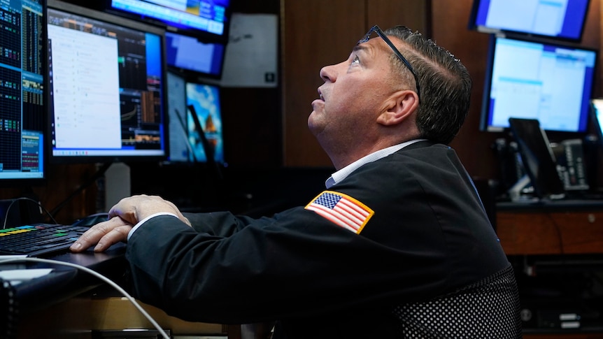a trader at the New York Stock Exchange looks up at a computer monitor from behind a desk