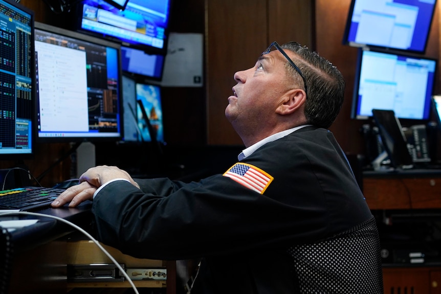 a trader at the New York Stock Exchange looks up at a computer monitor from behind a desk