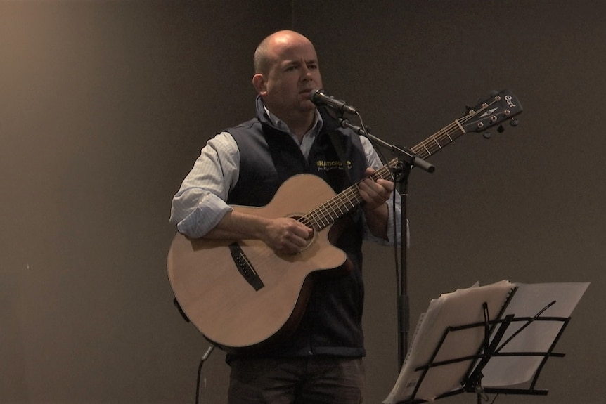 A man plays a guitar and sings