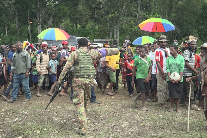 An armed soldier walks towards a crowd of voters pointing for them to move to one side.