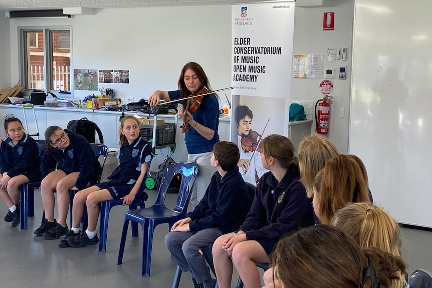 Woman stands behind row of seated students and plays violin.