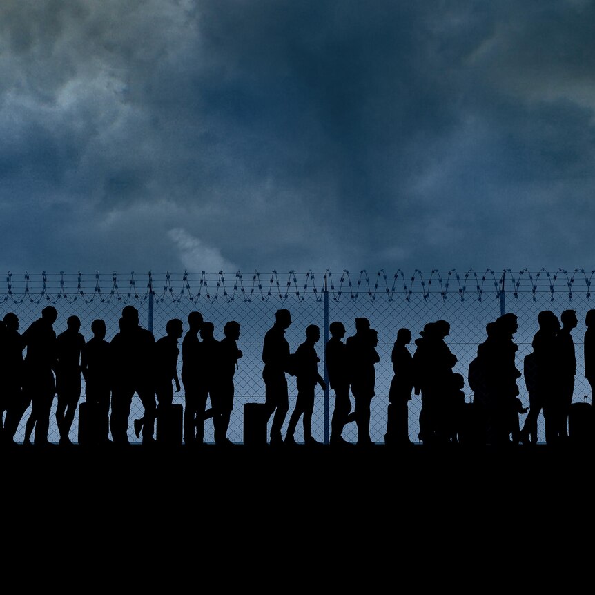 Silhouettes of dozens of people walking with bags and suitcases set against a razor wire fence and an overcast sky.