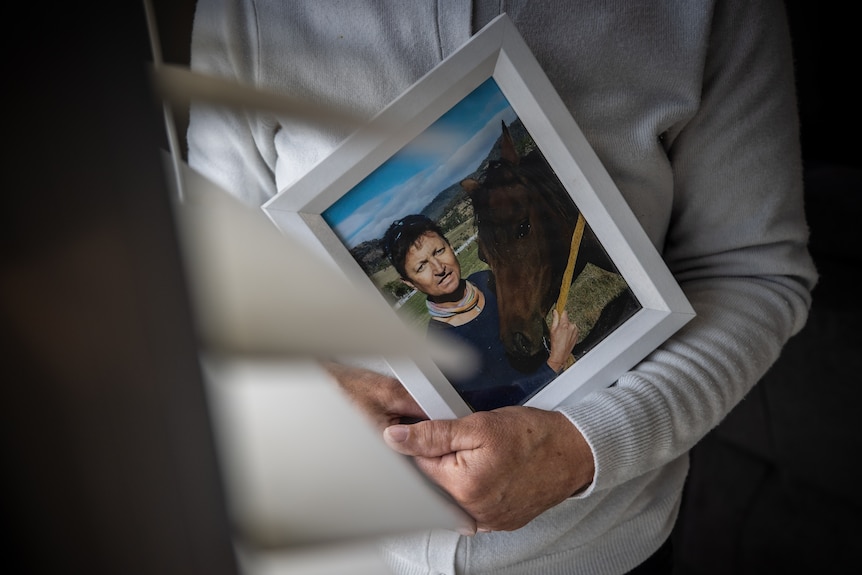 Obscured view of a person cradling a framed photograph of a person with a horse.