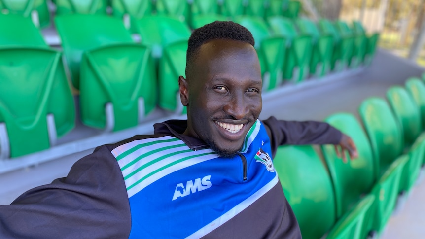 Friday Zico South Sudanese Australian Professional Footballer sitting in the grandstands smiling at the camera. 