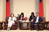 Nancy Pelosi, wearing a white suit and holding a microphone, sits in a leather chair across from a Taiwanese man in a navy suit.