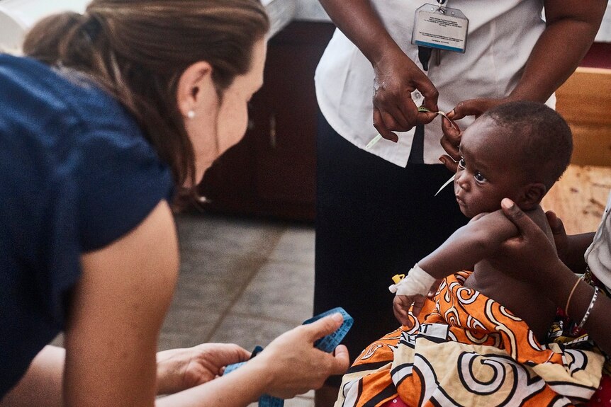 Dr phoebe williams holds a tape measure as she speaks to a young baby in the African country of Kenya