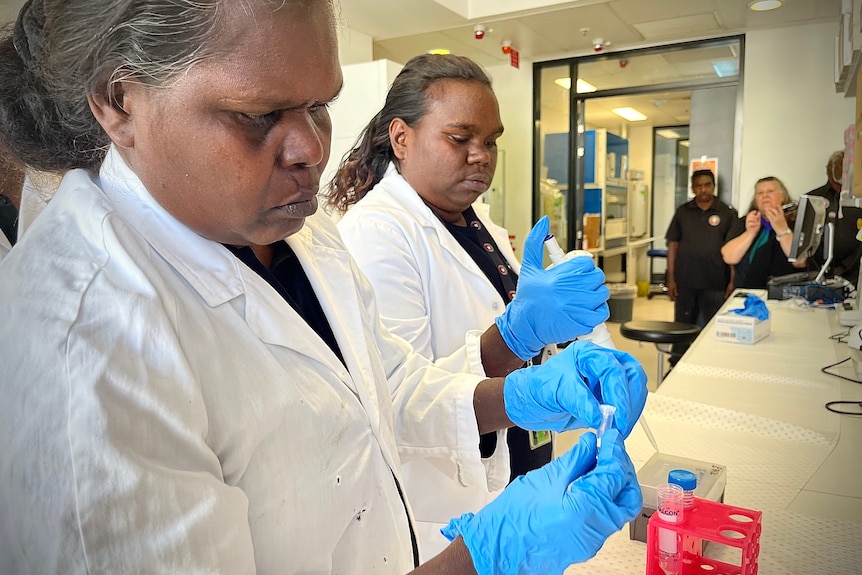 Two Galiwin'ku women wearing blue gloves and lab coats as they tour a university.