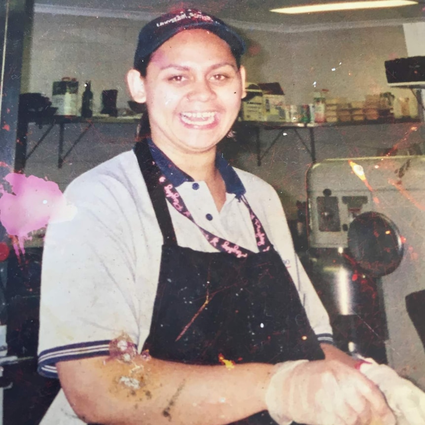 Nathalia with apron on in kitchen, smiling at camera, and stirring bowl