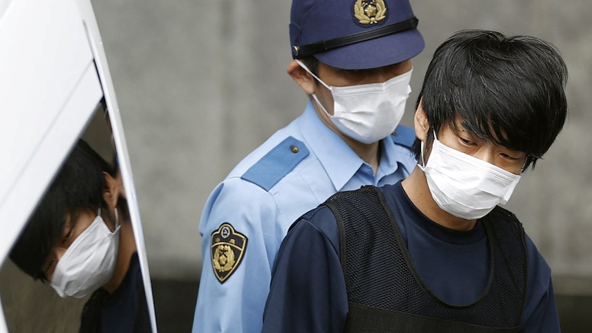 A young man wearing a face mask is held tightly by police
