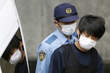 A young man wearing a face mask is held tightly by police