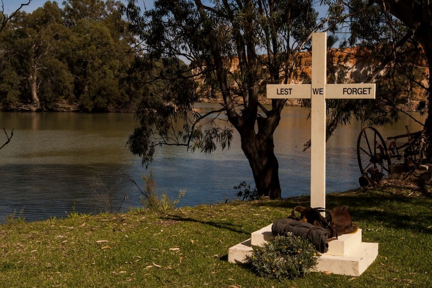 A cross with "Lest we Forget" written on it and a wreath laid beneath in front of a river.