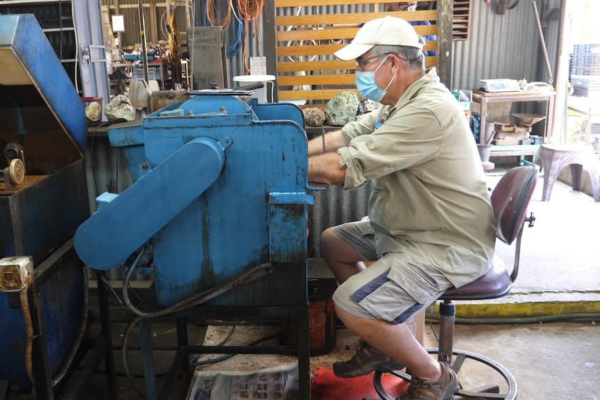 A man sits at a rock cutting machine