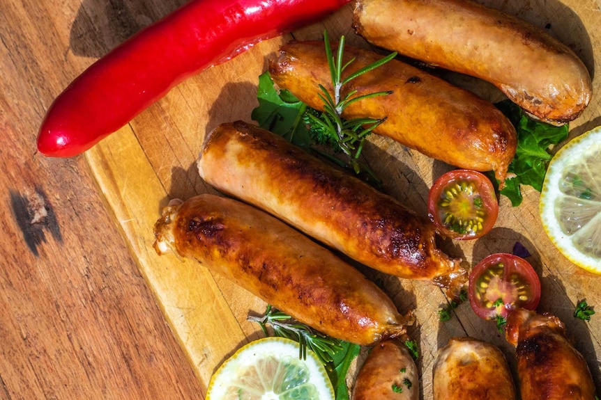 Seared sausages served on a wooden board garnished with lemon, chilli, tomato and rosemary
