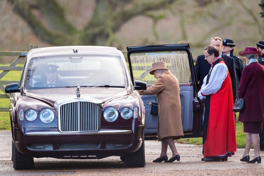the Queen starts to enter a black car with its door open as a group of people stand behind her
