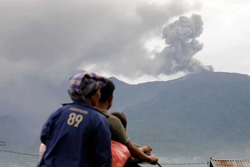 Motorists ride past by as Mount Marapi spews volcanic materials during its eruption in West Sumatra.