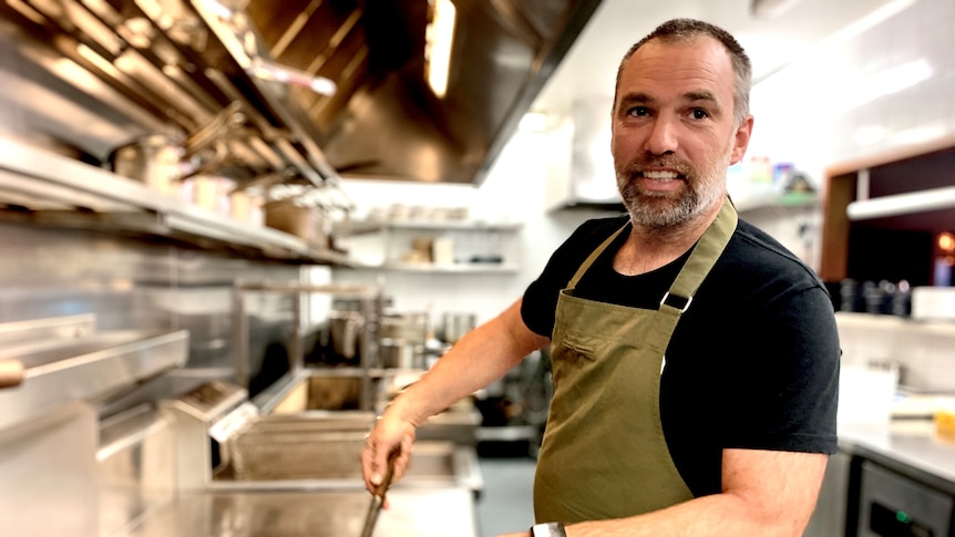 Restaurant owner Matt Upson stands at a stove wearing a khaki apron.