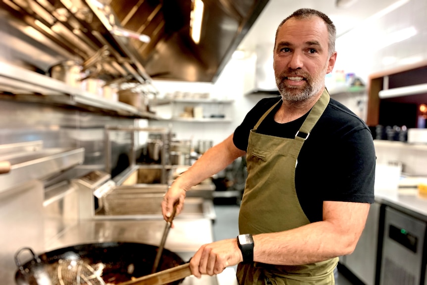 Restaurant owner Matt Upson stands at a stove wearing a khaki apron.