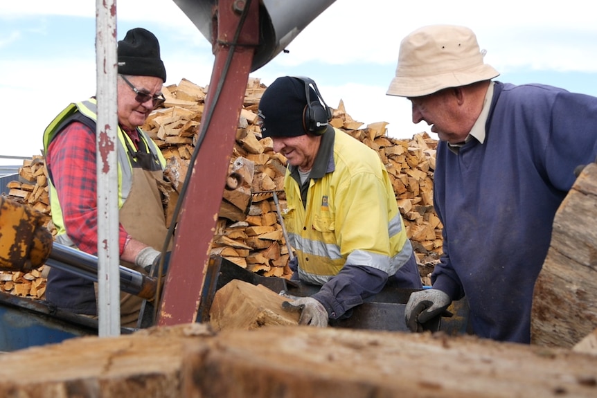 Three men stands around a man using an electric saw