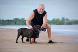 Man poses with dog on sand.