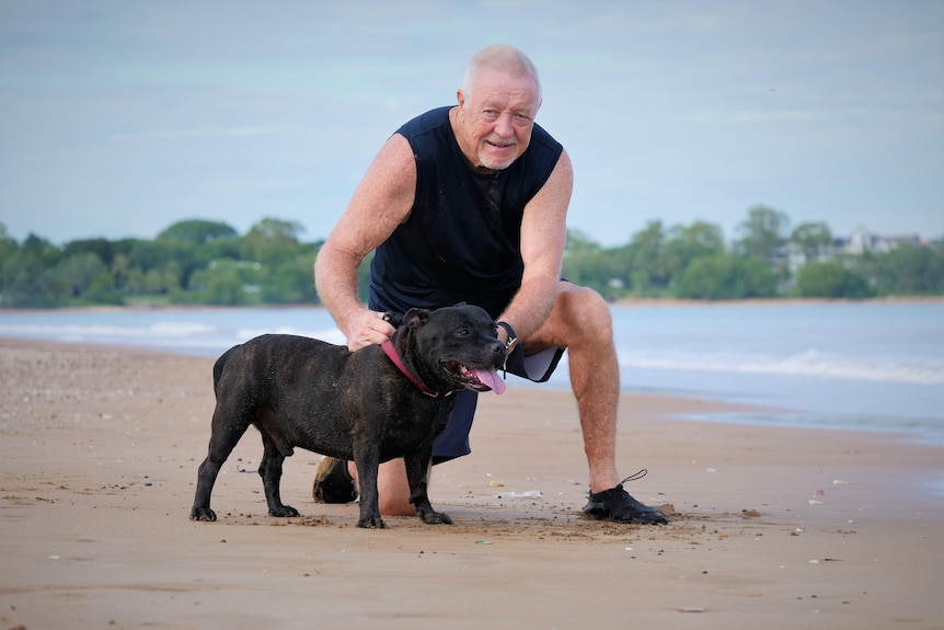 Man poses with dog on sand.