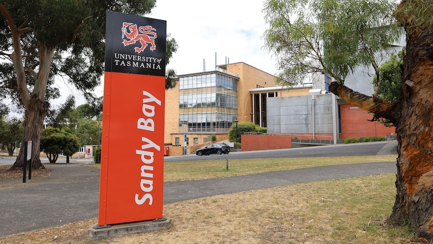 A red, white and black sign on a lawn that reads, University of Tasmania Sandy Bay