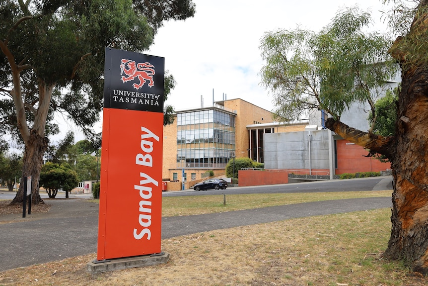 A red, white and black sign on a lawn that reads, University of Tasmania Sandy Bay