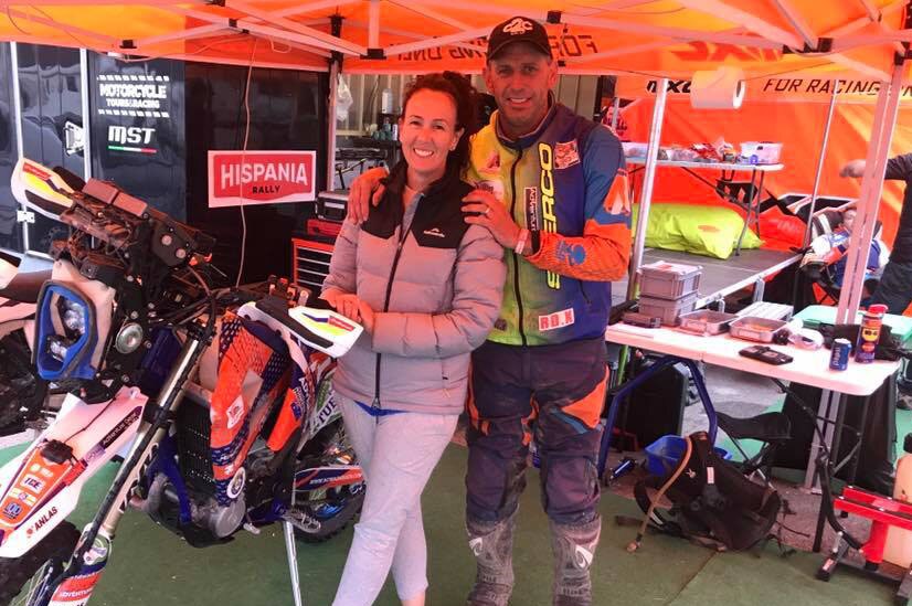 Man and woman standing next to a motorbike under a gazebo. The couple are looking at the camera.