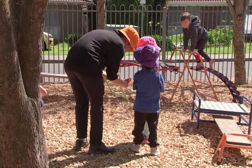 A preschool educator with three children in a playground.