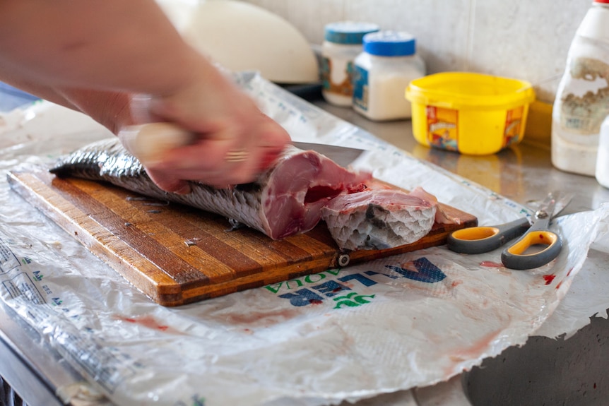 A person cutting a fish on a cutting board